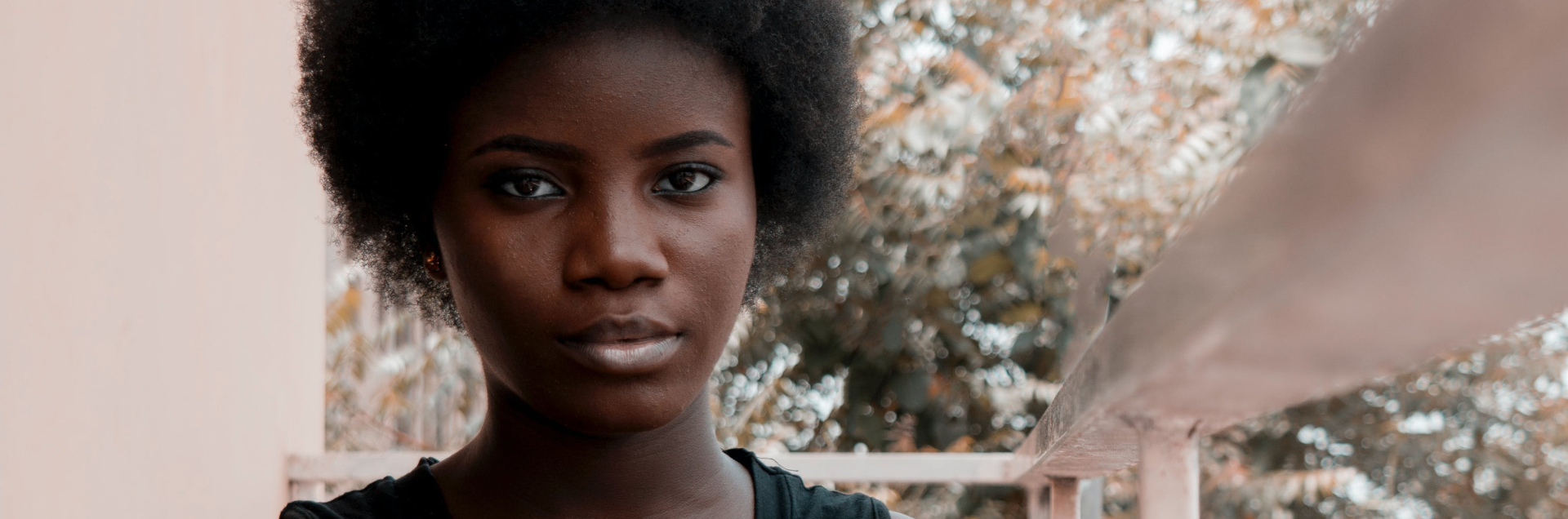 A young person outside directly facing the camera, with trees blurred in the background.