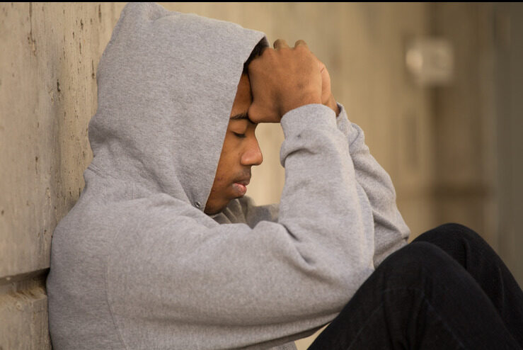 young person sitting against wall with their head in their hands